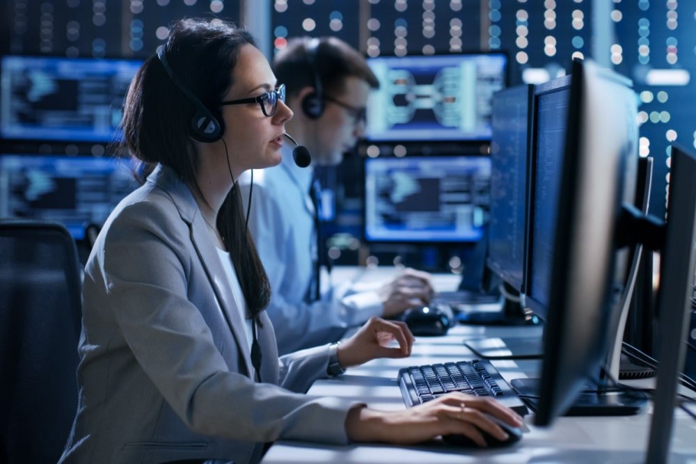 Support specialists wearing headsets at a multi-screen monitoring desk